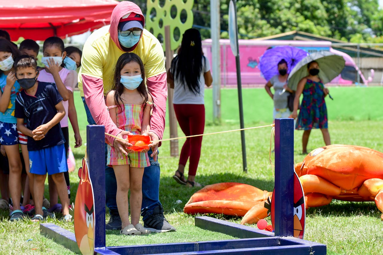 Children enjoying an outdoor game event while wearing face masks for safety.